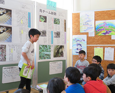 完成した新聞を張り出し、2年生にプレゼンする3年生=3月18日