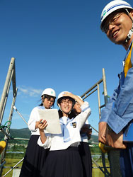 高さ１０メートルの足場の上で新幹線の取材をする新聞部の中野部長（中央）ら３人と山崎所長（右）