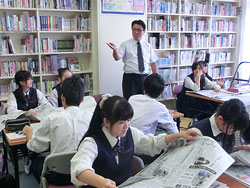 高橋教諭（中央奥）の指導で、新聞をめくって理不尽な事例を探す生徒たち 