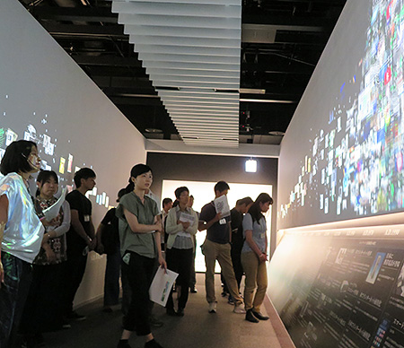 新聞を支えた技術を博物館内の情報のタイムトンネルを通りながら見学する教員たち